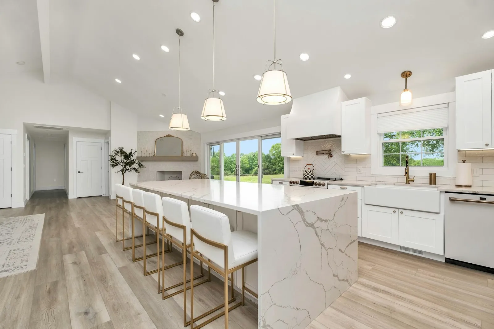 A bright white kitchen with a marble island, white bar stools and pendant lights