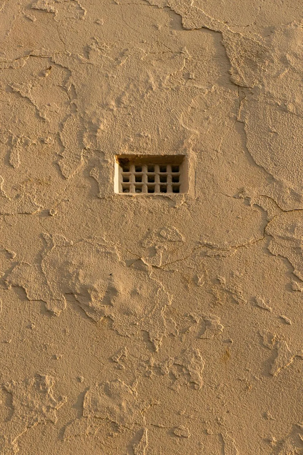 A small grilled vent opening in a tan stucco wall